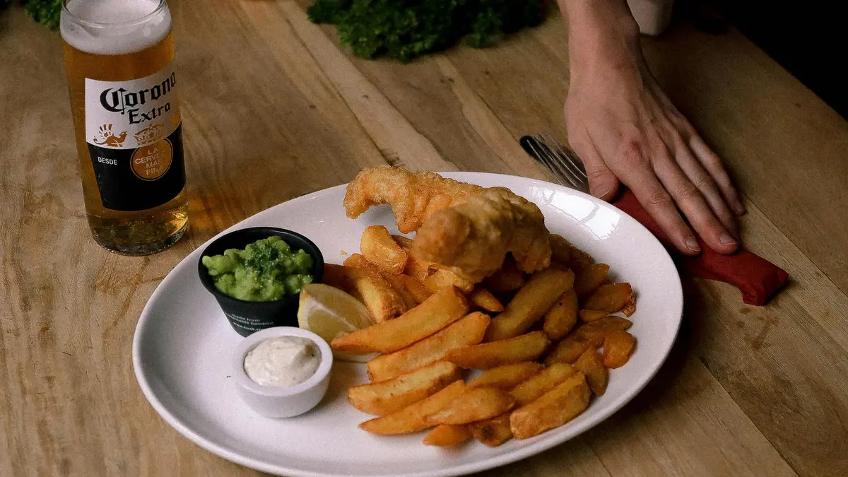 Fish and chips británico de bacalao rebozado con patatas, guisantes y limón